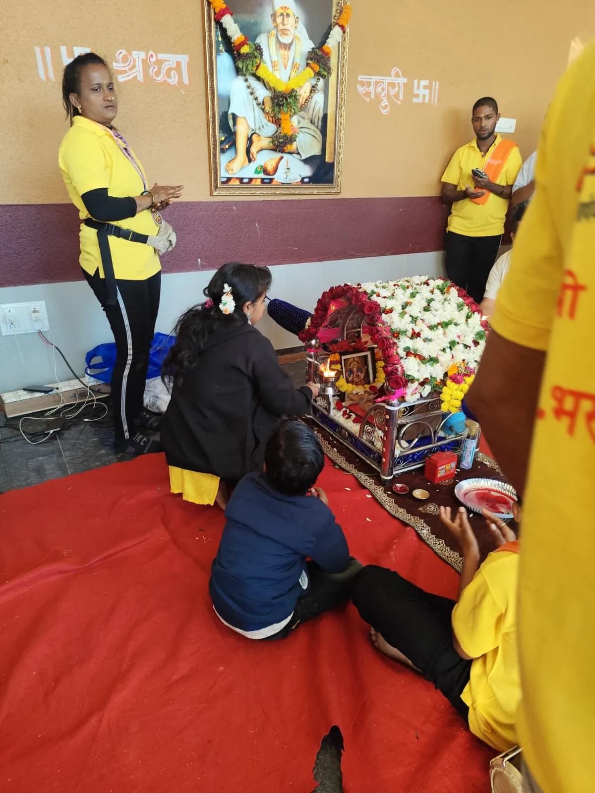 Devotees offering aarti before a floral palanquin and a portrait of Sai Baba